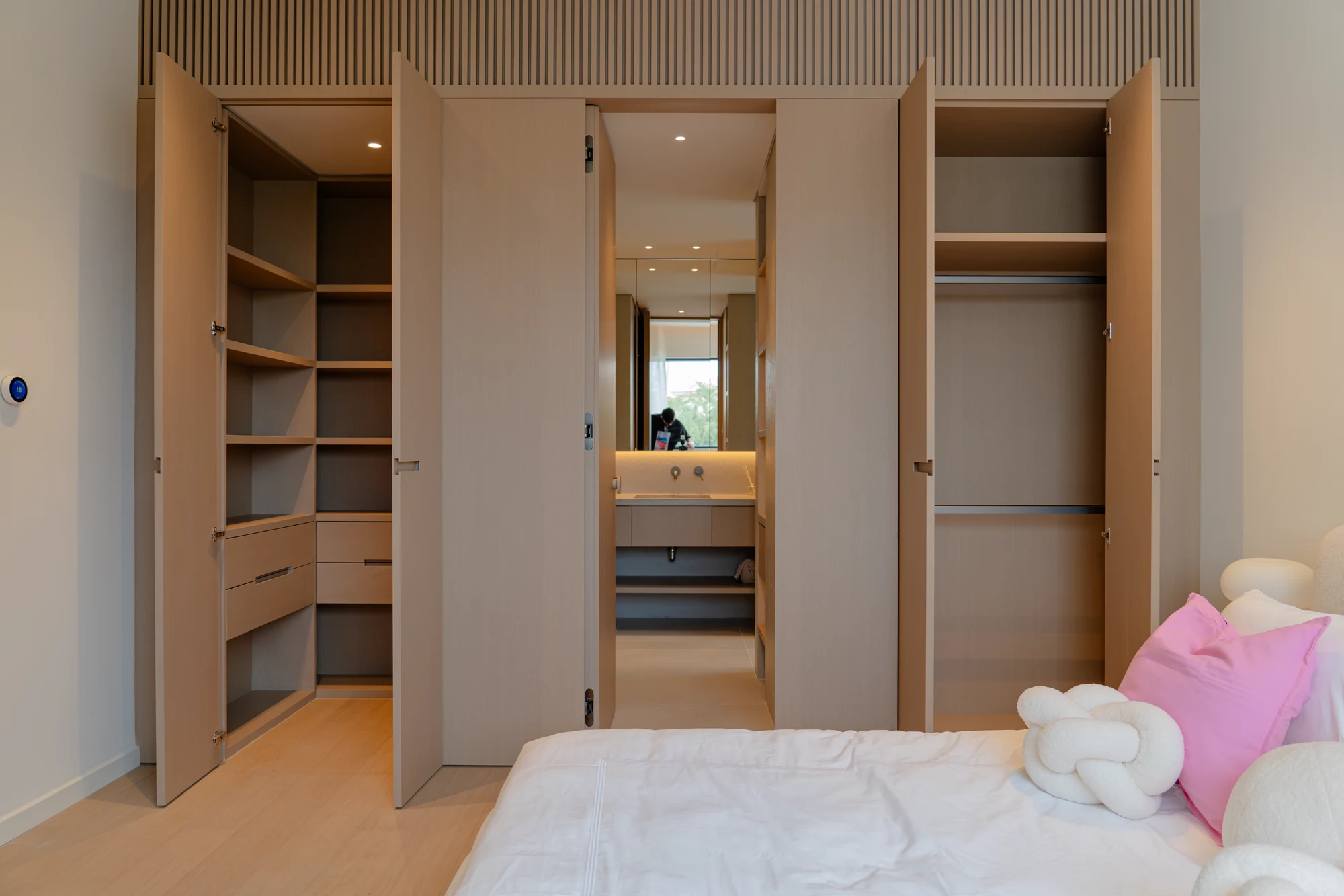 The same bedroom joinery opened to reveal shelving, drawers, hanging rails and the bathroom doorway