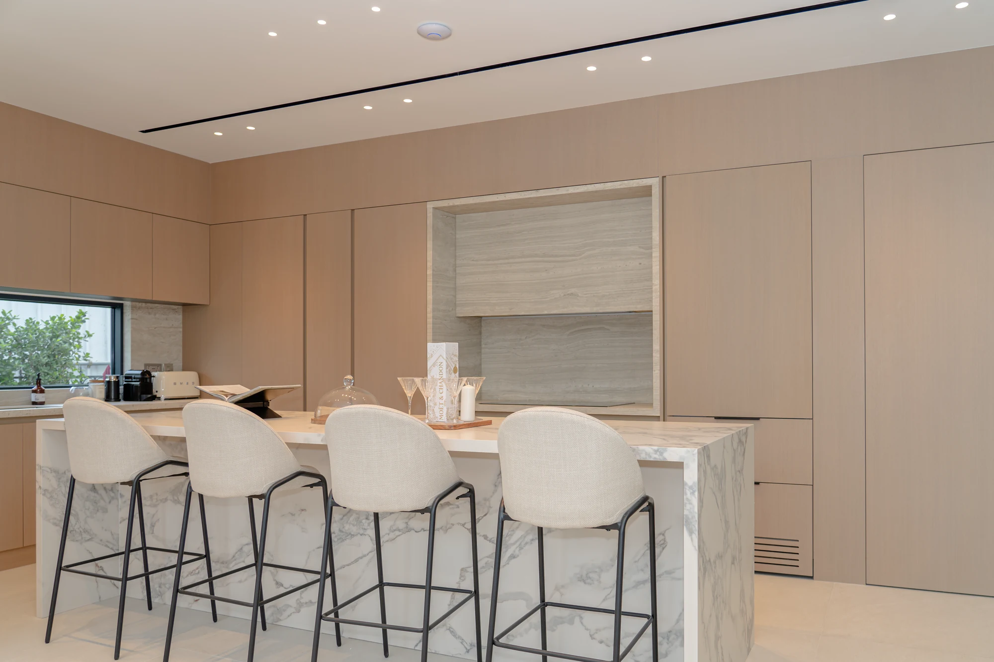 Kitchen with pale cabinetry, full-height panelling and a veined island with seating